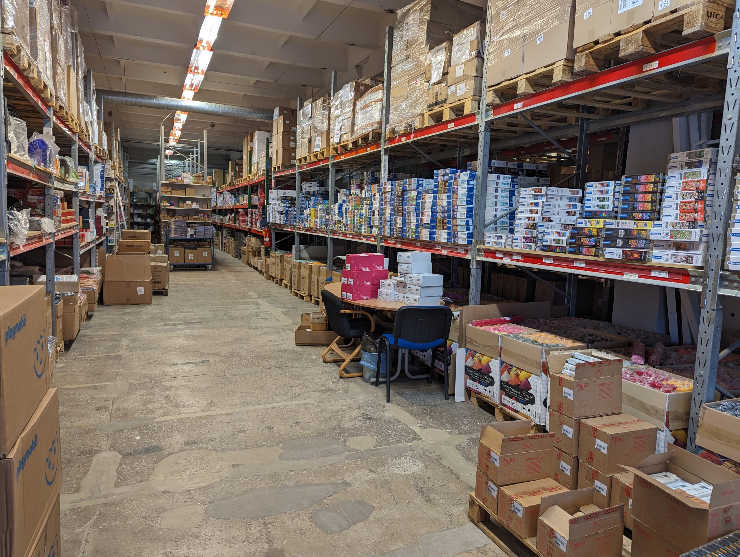 A warehouse aisle in Riga with pallet racks, stacked cartons and boxed goods on both sides.