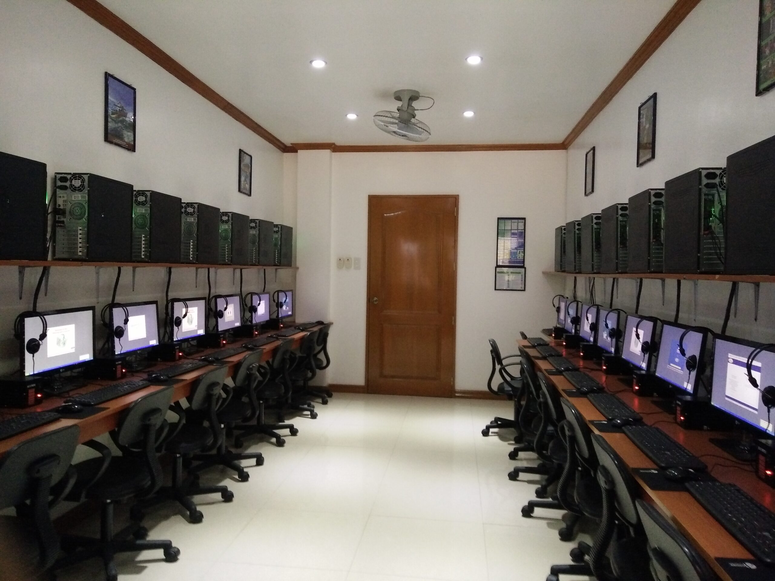 Empty training room with desktop computers and headsets arranged along two walls.