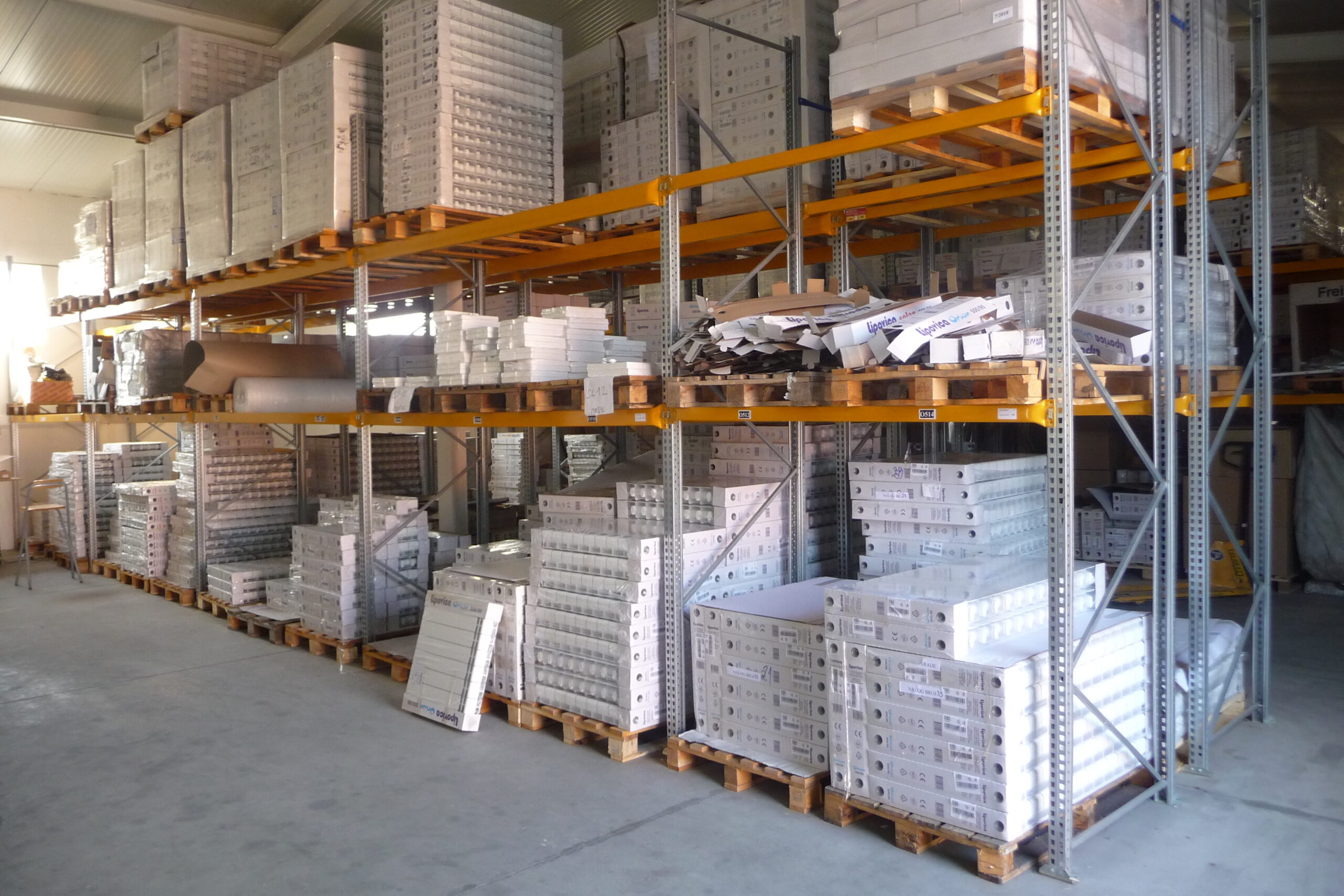 Packaged radiators stacked on pallets across several levels of metal warehouse shelving.