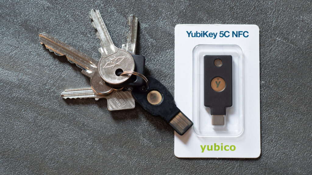 A hardware security key attached to metal keys beside a packaged YubiKey 5C NFC on a dark surface.